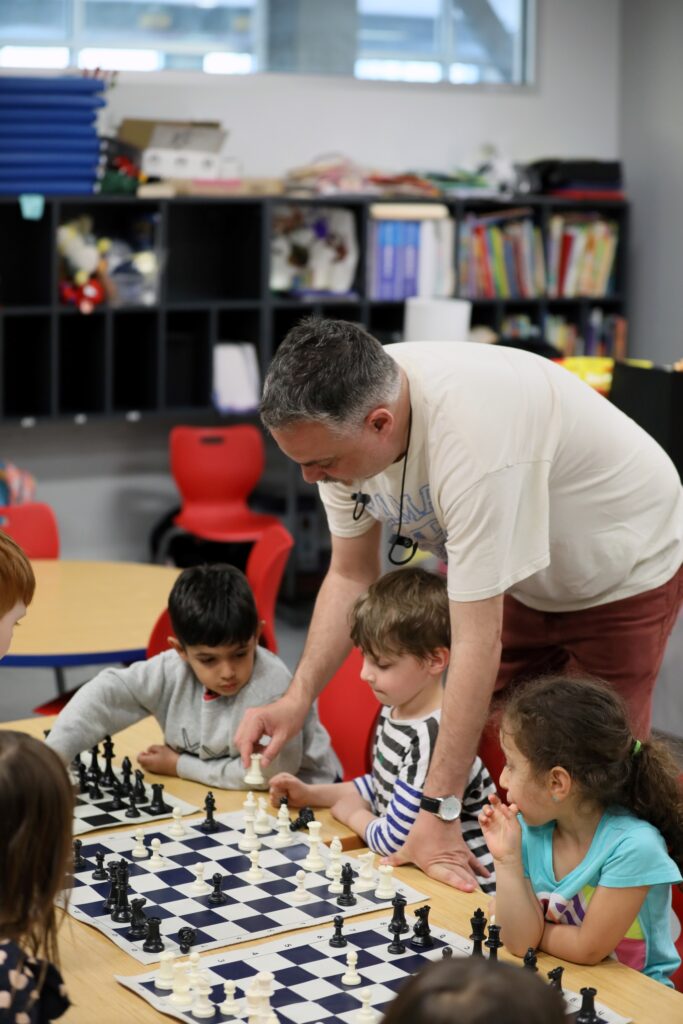 Teacher and students looking at chess boards while playing chess.