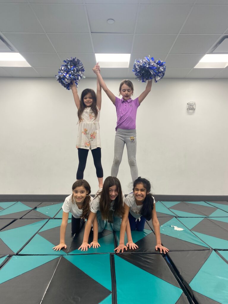 girl students make cheer gymnastics pyramid with pompoms