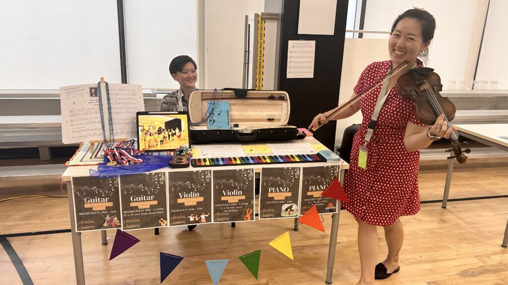 woman with violin in front of a table of musical materials at the extracurricular fair