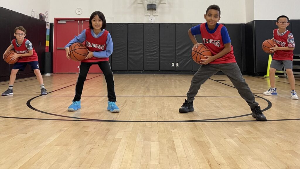 four lower school boy students stand in basketball poses wearing their wildcat jerseys