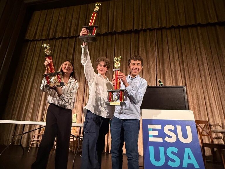 three middle school students hold up their championship trophies at the ESU USA speech and debate tournament in new york city
