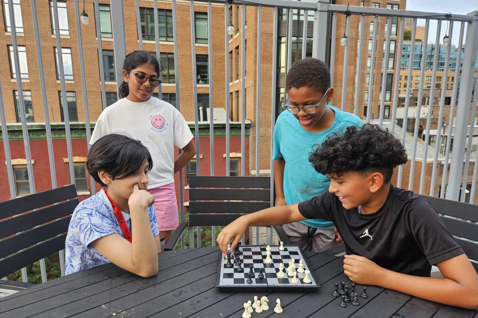 four students playing chess and socializing on the roof