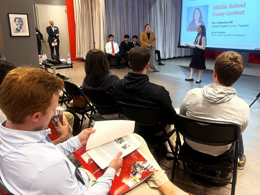 female student presents her winning essay overview with a teacher standing next to her in front of an audience