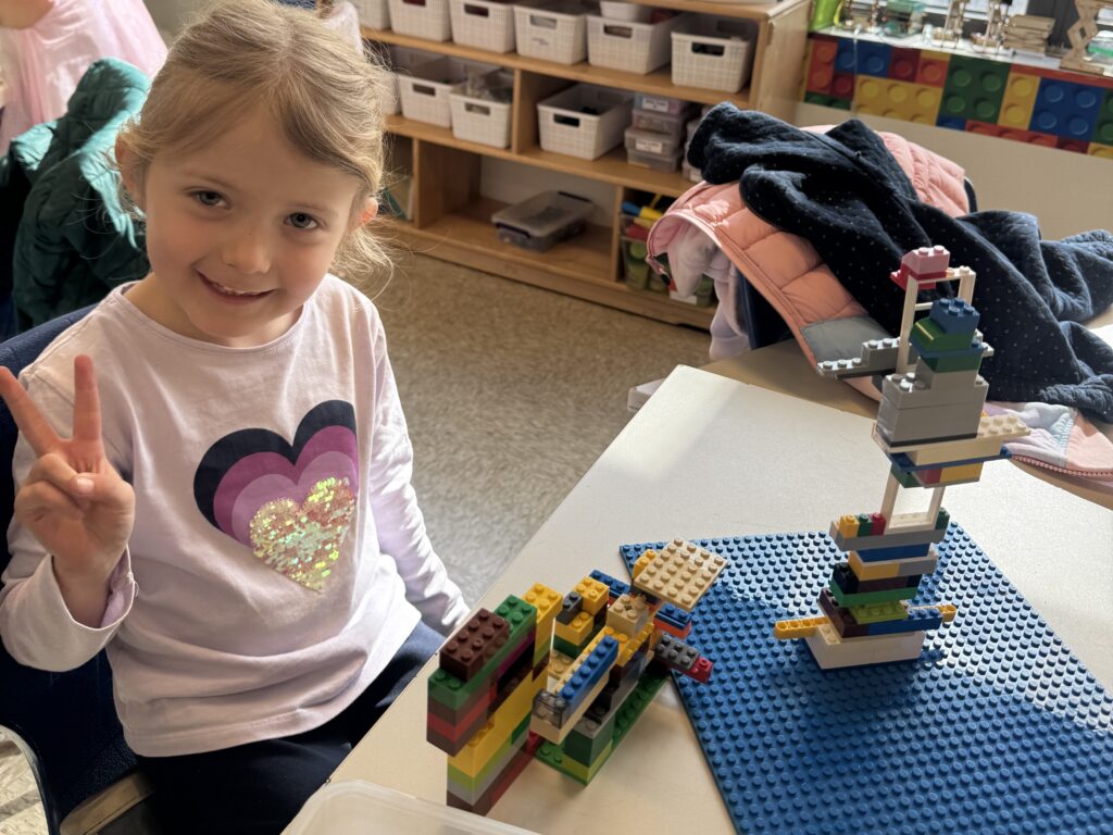 female student sits at a table and smiles with LEGO structures that look like a space launch system in front of her.